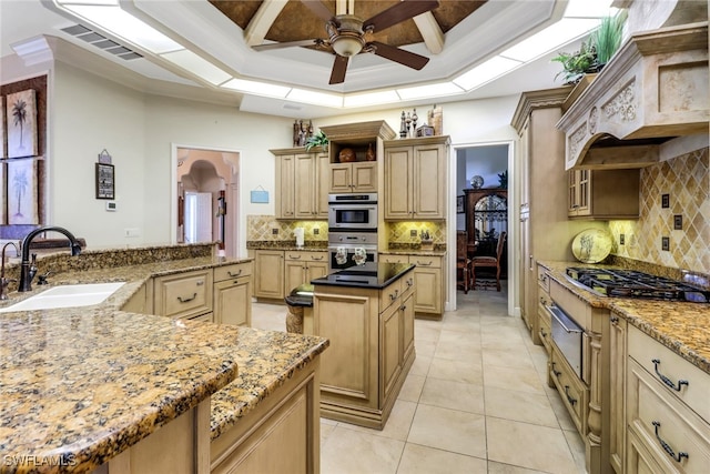 kitchen featuring gas stovetop, a raised ceiling, visible vents, a kitchen island, and a sink