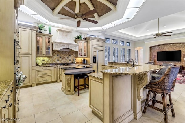 kitchen with cream cabinetry, custom exhaust hood, appliances with stainless steel finishes, a large island with sink, and a kitchen bar