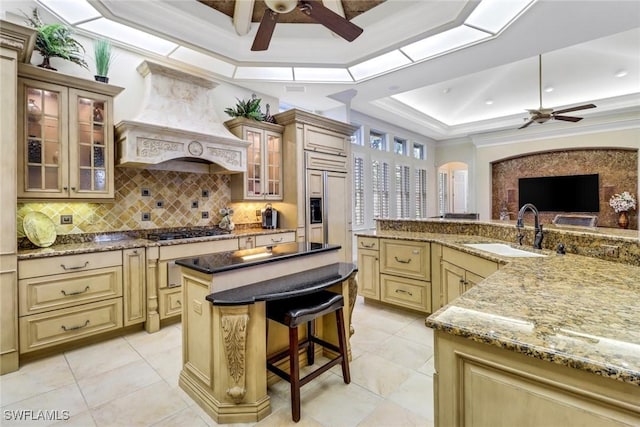 kitchen with paneled built in fridge, a raised ceiling, cream cabinets, premium range hood, and a sink