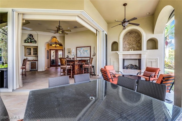 view of patio / terrace featuring a large fireplace, beverage cooler, outdoor dining area, and a ceiling fan