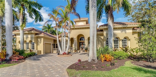 mediterranean / spanish home featuring an attached garage, french doors, decorative driveway, and stucco siding