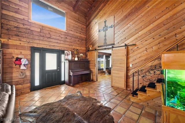 foyer with a high ceiling, light tile patterned flooring, a barn door, and wood walls