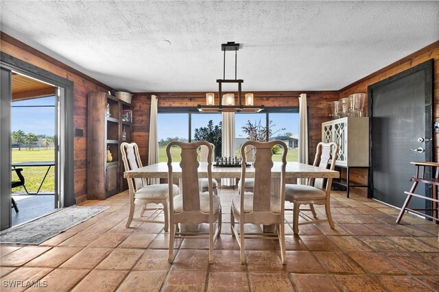 dining area with an inviting chandelier, a textured ceiling, and wood walls