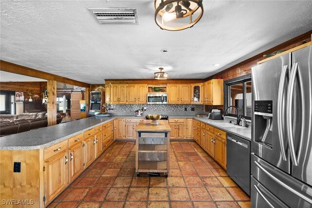 kitchen featuring appliances with stainless steel finishes, tasteful backsplash, sink, a center island, and a textured ceiling