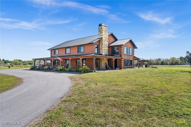 view of front of house with metal roof, driveway, log exterior, a chimney, and a front yard