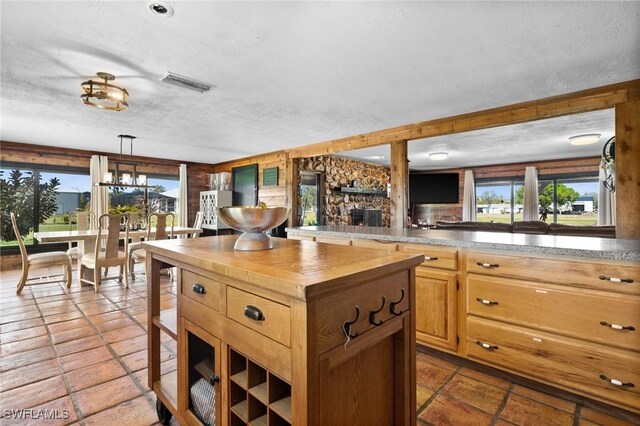 kitchen featuring plenty of natural light, a stone fireplace, hanging light fixtures, and a textured ceiling