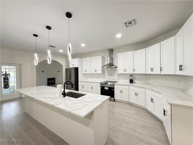 kitchen with appliances with stainless steel finishes, sink, white cabinetry, a kitchen island with sink, and wall chimney range hood