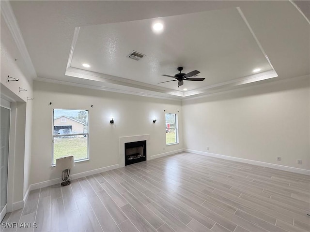 unfurnished living room featuring light hardwood / wood-style floors, a tray ceiling, crown molding, and ceiling fan