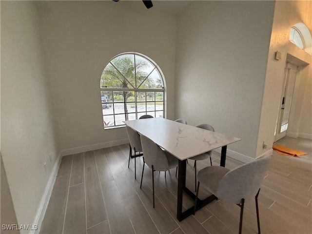 dining space featuring a towering ceiling, ceiling fan, and light hardwood / wood-style flooring