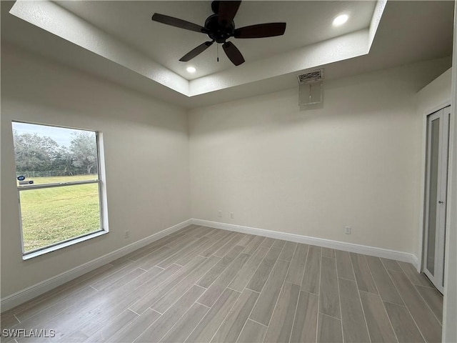 empty room with light hardwood / wood-style floors, a tray ceiling, and ceiling fan