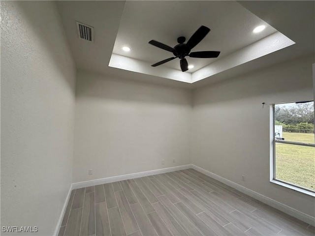 empty room featuring ceiling fan, light hardwood / wood-style flooring, and a tray ceiling