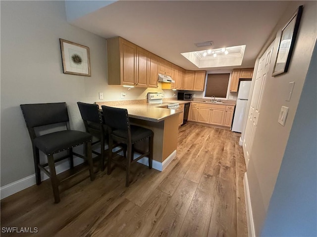 kitchen featuring white appliances, a kitchen breakfast bar, a tray ceiling, light brown cabinetry, and kitchen peninsula