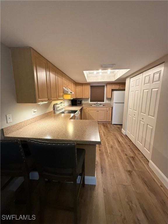 kitchen featuring white appliances, a kitchen breakfast bar, wood-type flooring, a raised ceiling, and kitchen peninsula