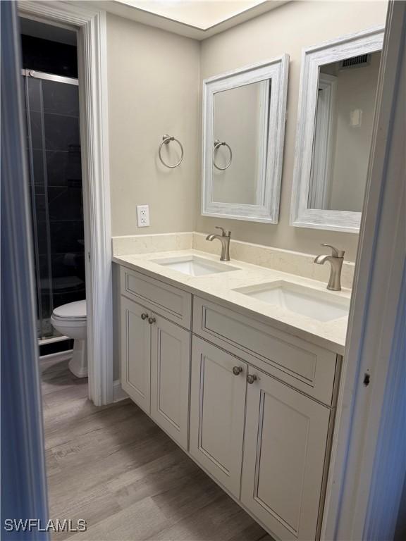 bathroom featuring vanity, hardwood / wood-style flooring, a shower with door, and toilet