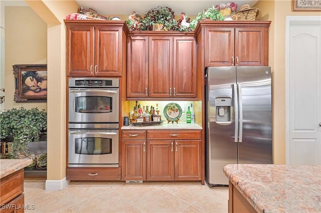 kitchen with appliances with stainless steel finishes, light tile patterned floors, and light stone counters