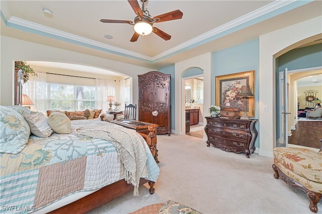 bedroom with ensuite bath, ceiling fan, ornamental molding, light carpet, and a raised ceiling