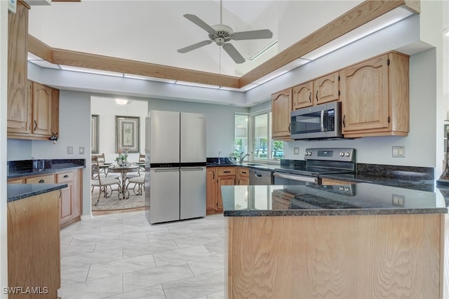 kitchen featuring kitchen peninsula, ceiling fan, appliances with stainless steel finishes, dark stone countertops, and lofted ceiling