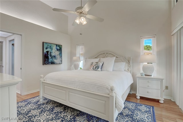 bedroom with light hardwood / wood-style floors, a towering ceiling, and ceiling fan