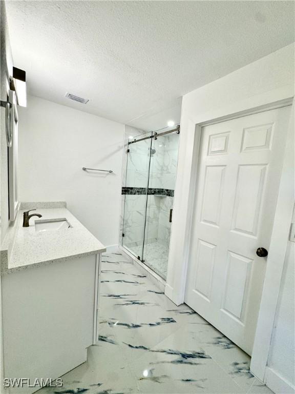 bathroom with vanity, a textured ceiling, and a shower with shower door