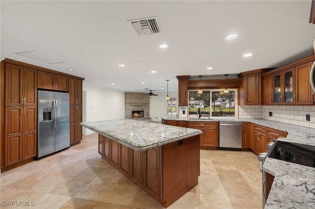 kitchen featuring appliances with stainless steel finishes, decorative light fixtures, a stone fireplace, light stone counters, and decorative backsplash