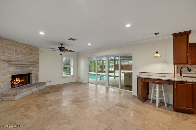 unfurnished living room featuring ceiling fan, sink, ornamental molding, and a fireplace