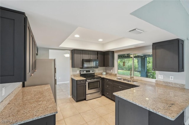 kitchen with appliances with stainless steel finishes, sink, kitchen peninsula, a raised ceiling, and light stone countertops