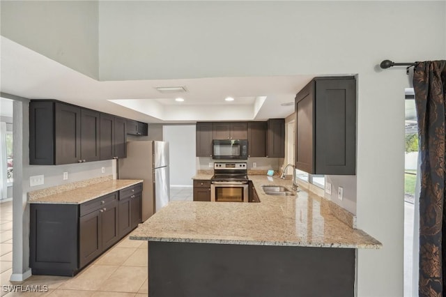 kitchen featuring sink, light tile patterned floors, appliances with stainless steel finishes, a tray ceiling, and kitchen peninsula