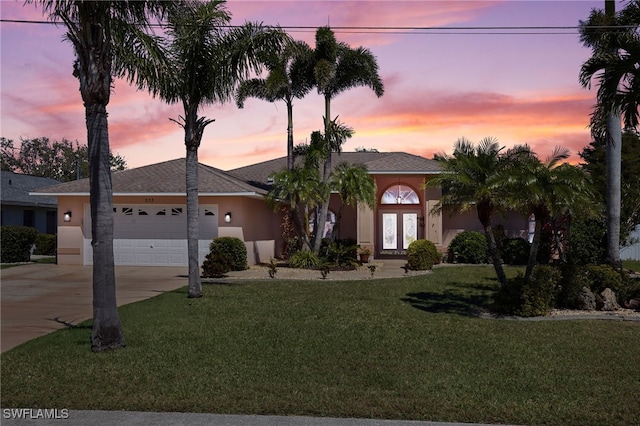 ranch-style house featuring concrete driveway, stucco siding, french doors, a yard, and an attached garage