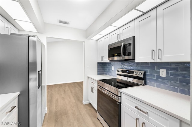 kitchen with tasteful backsplash, white cabinetry, light hardwood / wood-style floors, and appliances with stainless steel finishes