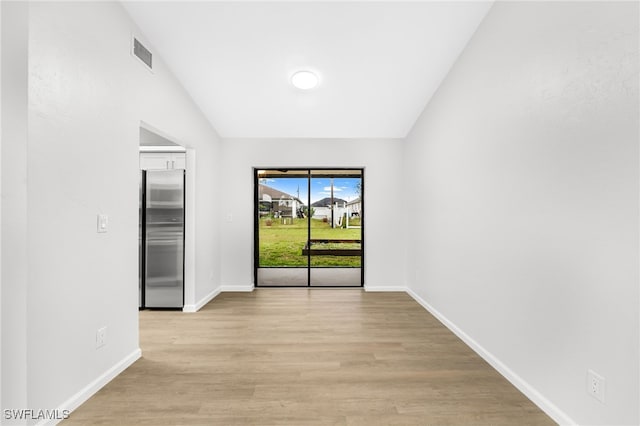 unfurnished room with light wood-type flooring and vaulted ceiling