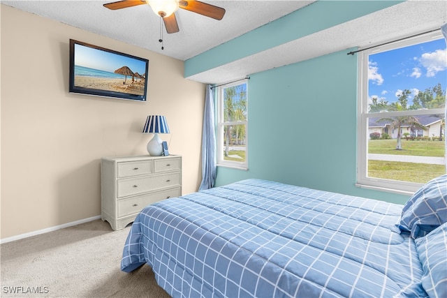 bedroom with ceiling fan, light colored carpet, and a textured ceiling