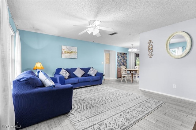 living room featuring ceiling fan with notable chandelier, wood-type flooring, and a textured ceiling