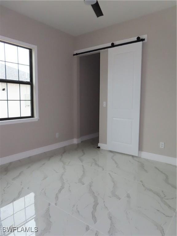 unfurnished bedroom featuring a barn door and ceiling fan