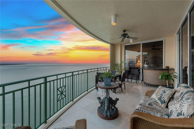 balcony at dusk with a water view and ceiling fan