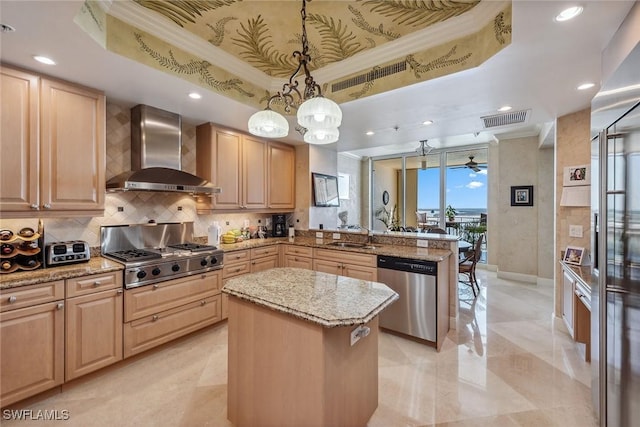 kitchen featuring wall chimney exhaust hood, a center island, a tray ceiling, pendant lighting, and stainless steel appliances