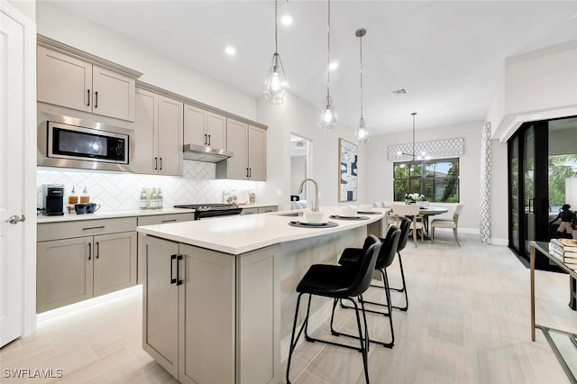 kitchen with pendant lighting, sink, gray cabinets, a kitchen island with sink, and stainless steel appliances