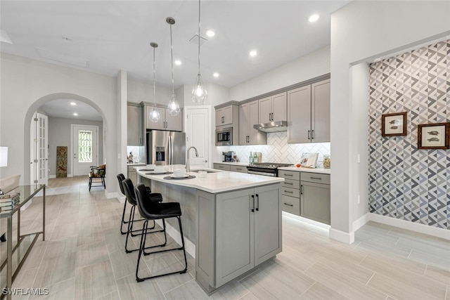 kitchen featuring gray cabinets, sink, hanging light fixtures, stainless steel appliances, and a center island with sink