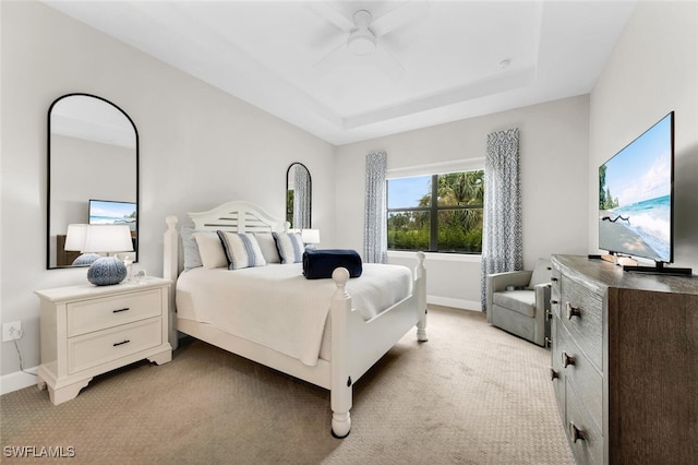 carpeted bedroom with a raised ceiling and ceiling fan