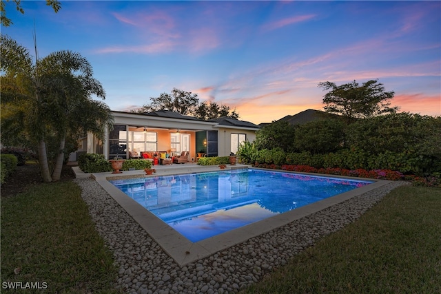 pool at dusk with a patio and a lawn