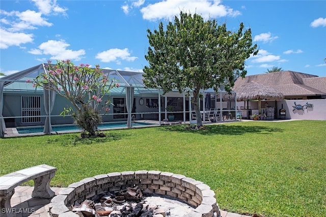 rear view of property featuring a yard, glass enclosure, and a fire pit