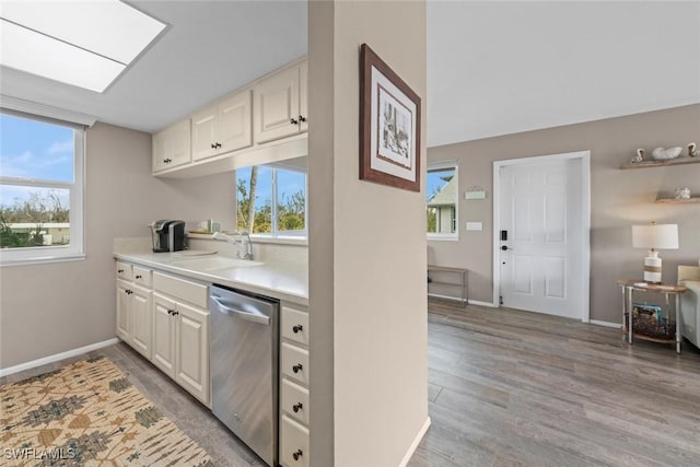 kitchen with sink, white cabinetry, a skylight, light hardwood / wood-style floors, and stainless steel dishwasher
