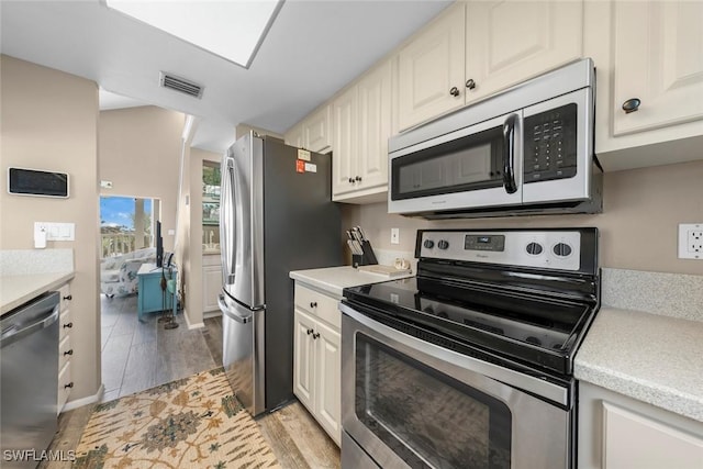 kitchen with stainless steel appliances, light hardwood / wood-style floors, and white cabinets