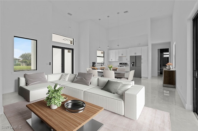 living room with a high ceiling, a healthy amount of sunlight, sink, and french doors