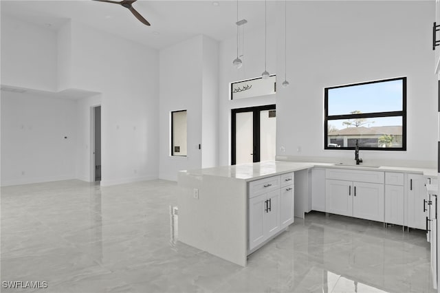 kitchen featuring sink, white cabinetry, hanging light fixtures, kitchen peninsula, and a towering ceiling