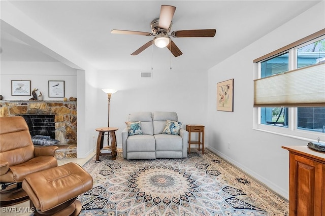 living area featuring a stone fireplace and ceiling fan