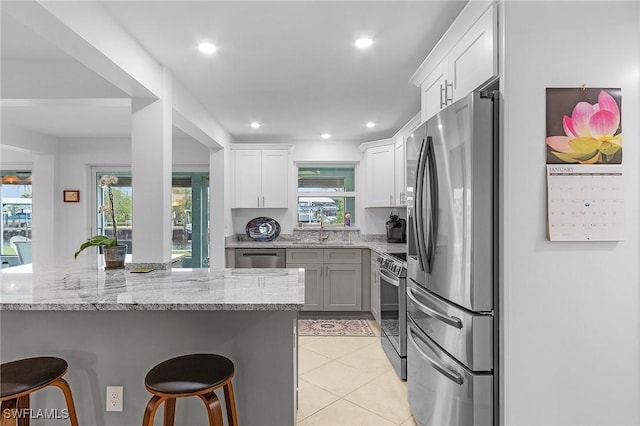 kitchen featuring a breakfast bar, white cabinetry, light tile patterned floors, appliances with stainless steel finishes, and light stone countertops