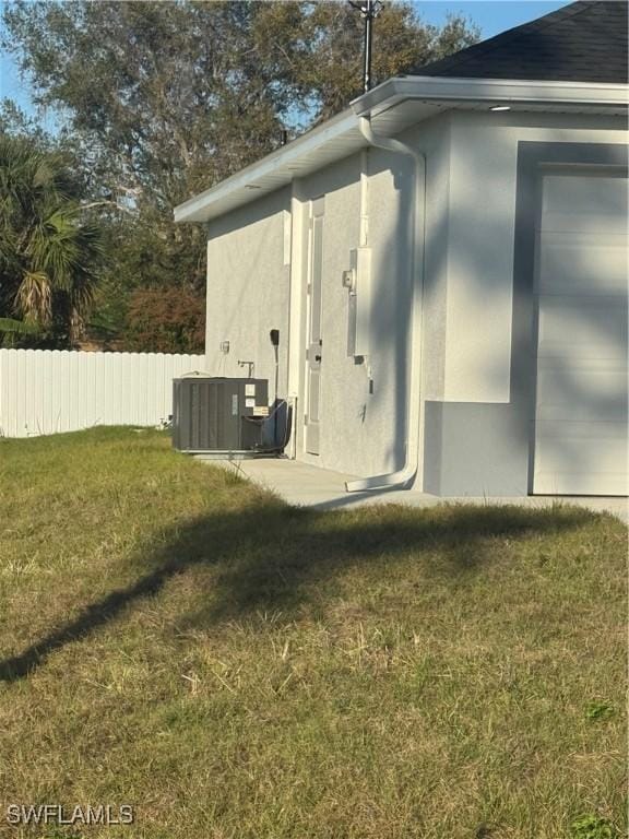 view of property exterior featuring central AC unit, a lawn, fence, and stucco siding