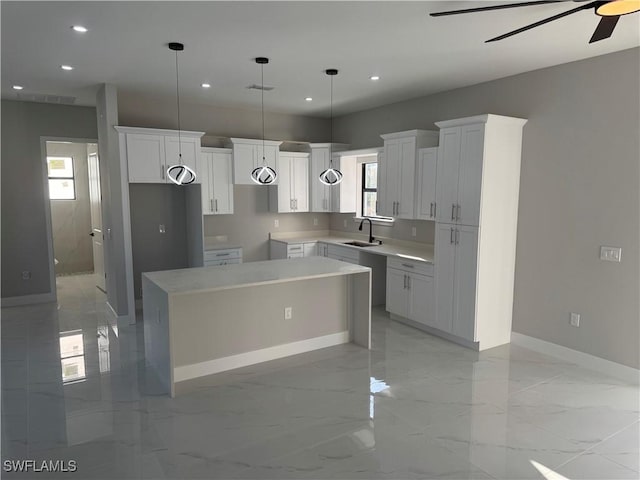 kitchen with decorative light fixtures, light countertops, white cabinetry, a kitchen island, and a sink