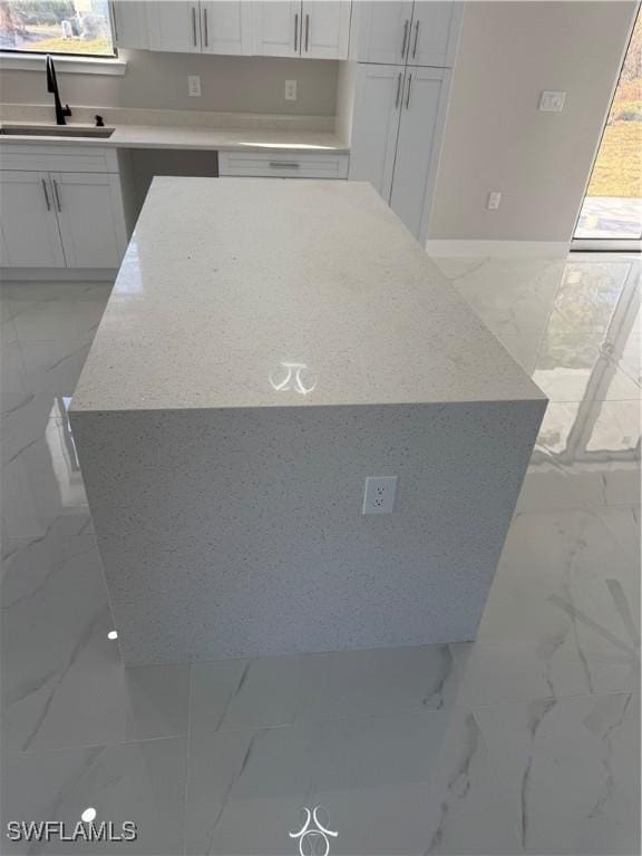 kitchen with light stone counters, marble finish floor, white cabinets, and a sink