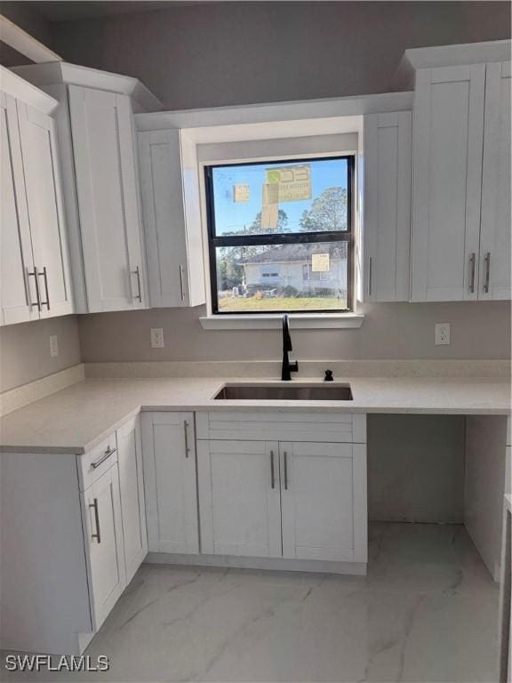 kitchen featuring marble finish floor, light countertops, a sink, and white cabinets